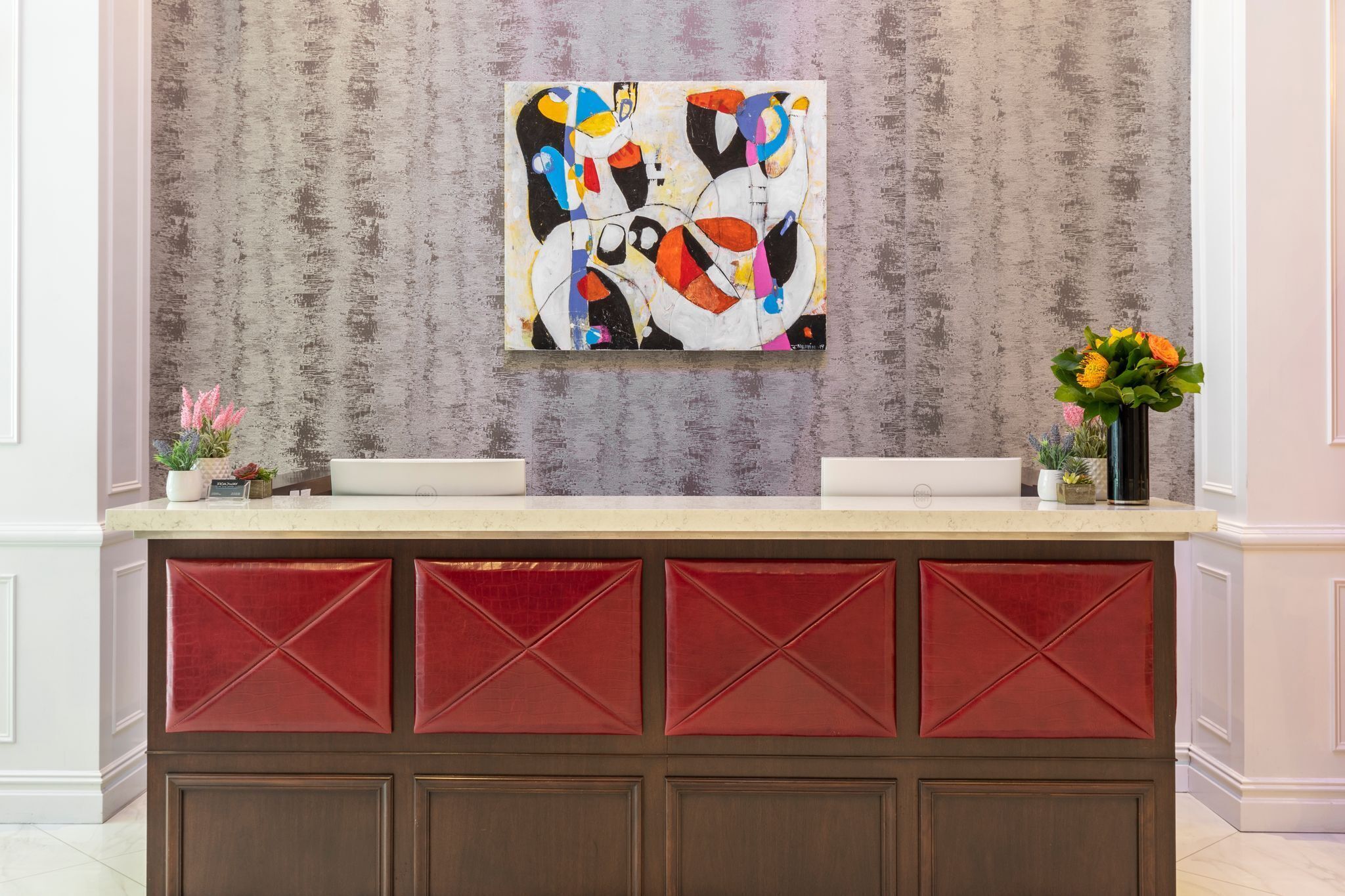 Un espace d’accueil au design moderne, agrément é d’un grand tableau abstrait au mur, d’un comptoir blanc et de sièges rembourrés de couleur rouge.