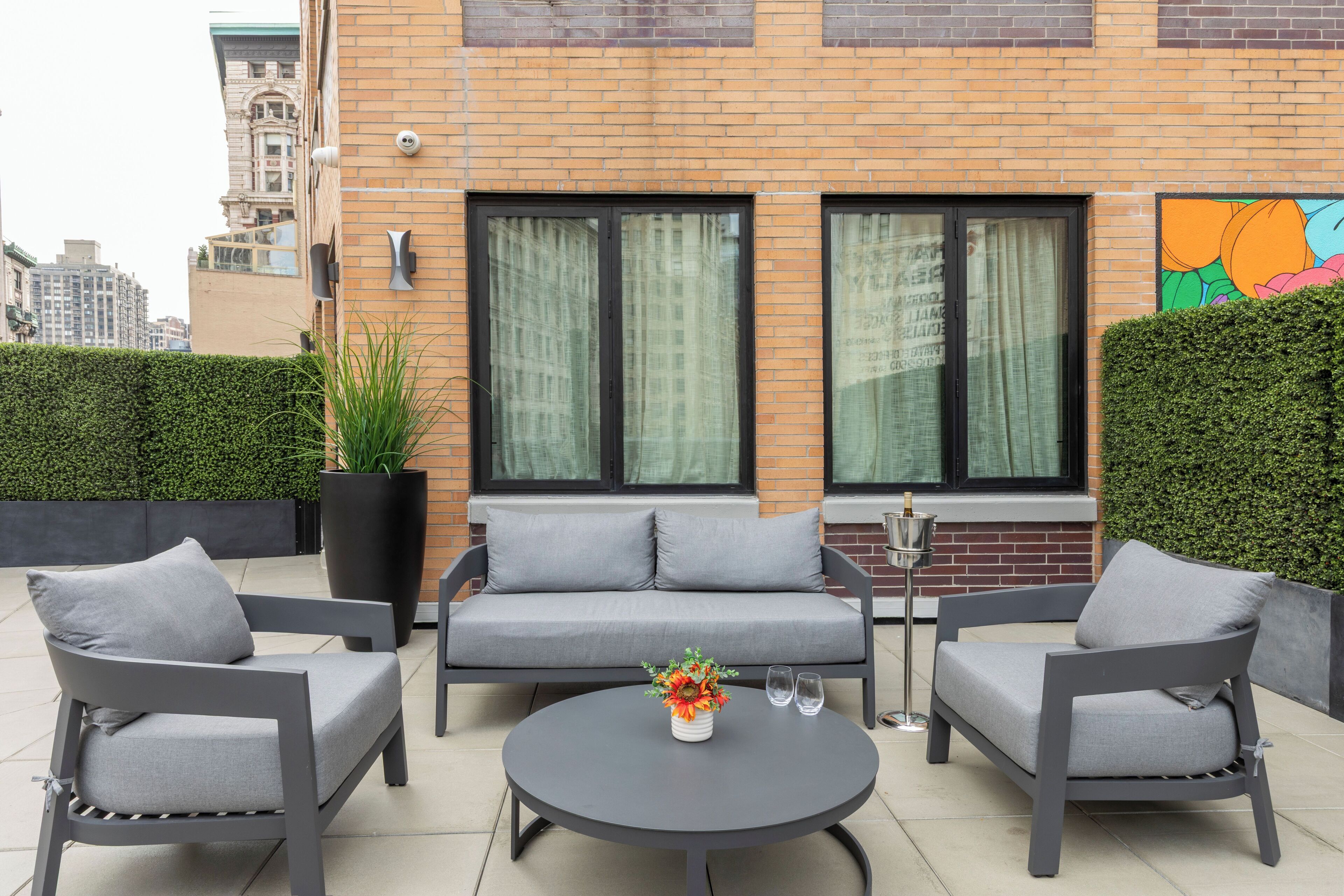 Un espace extérieur moderne, aménagé avec un canapé et deux fauteuils, une table ronde et une plante en pot.
