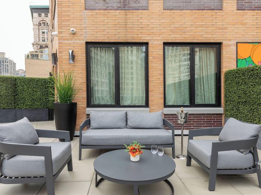 Un espace extérieur moderne, aménagé avec un canapé et deux fauteuils, une table ronde et une plante en pot.