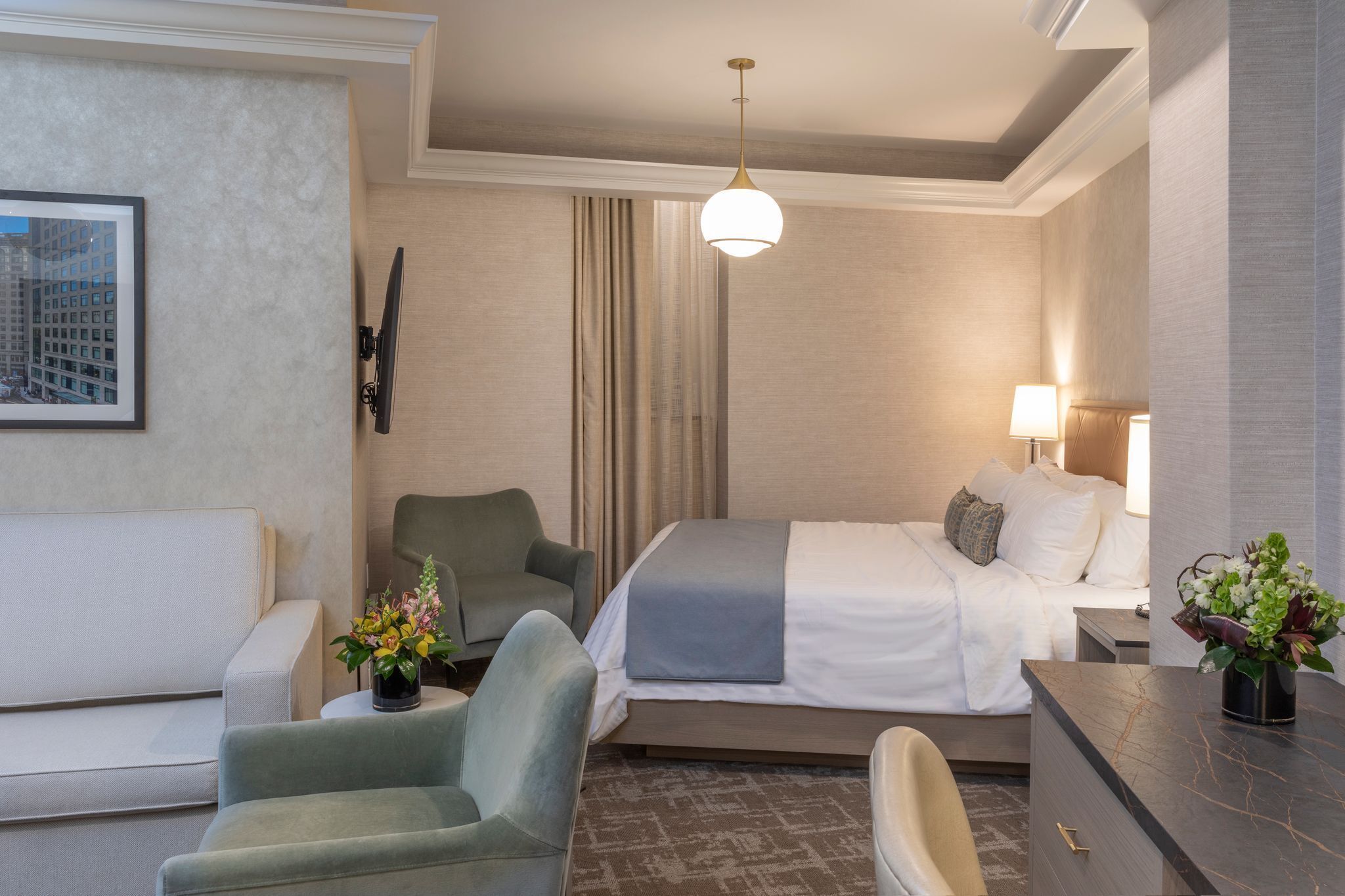 A hotel room with a bed, a sofa, a desk, a chair, a TV, a lamp, and a framed picture on the wall.