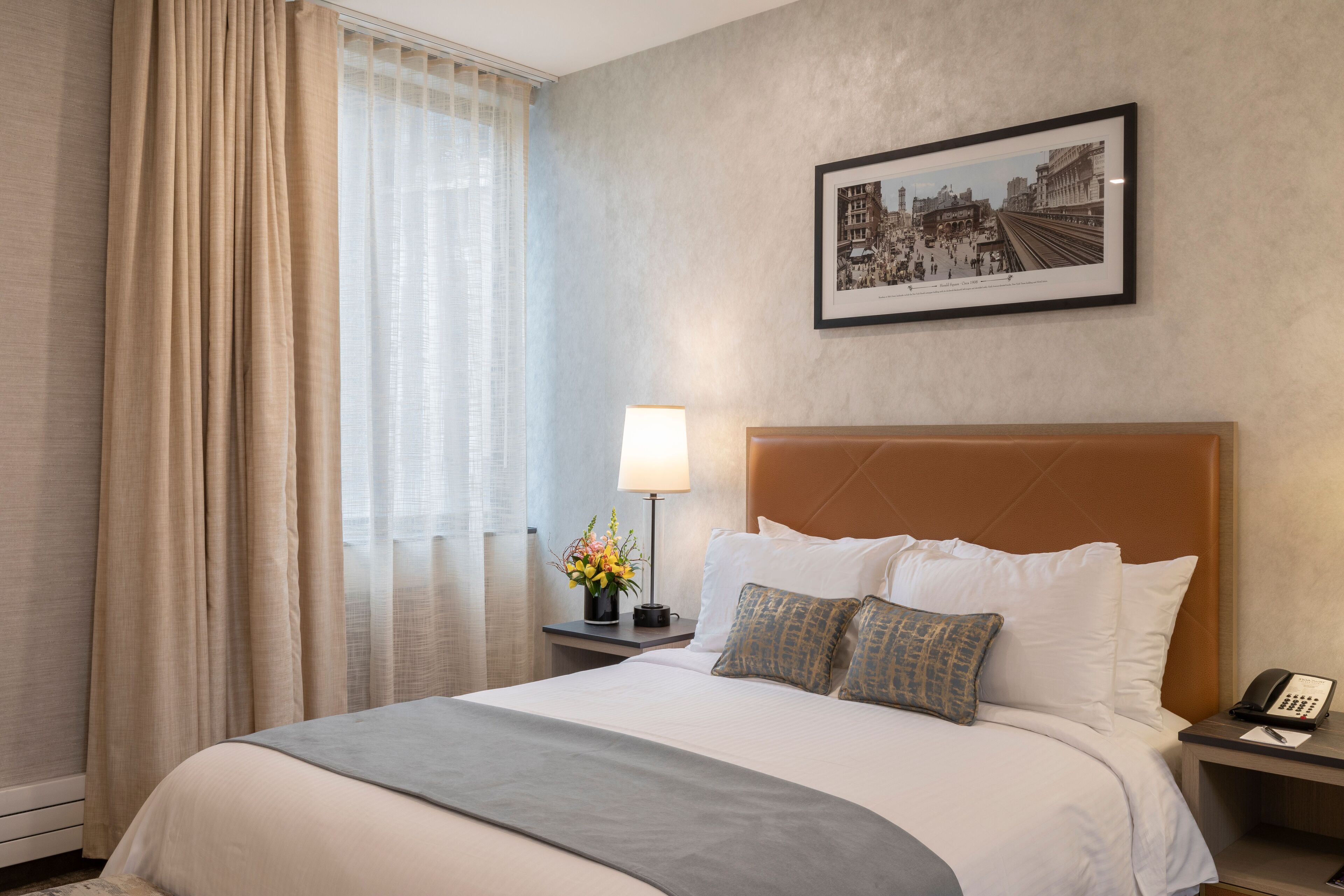 Ein Hotelzimmer mit einem großen Bett, einem Nachttisch mit Lampe, einem gerahmten Bild an der Wand und einem Fenster mit Vorhängen.