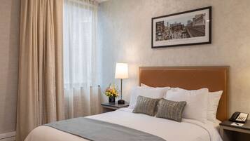 Ein Hotelzimmer mit einem großen Bett, einem Nachttisch mit Lampe, einem gerahmten Bild an der Wand und einem Fenster mit Vorhängen.