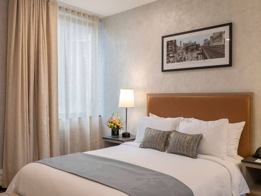 Ein Hotelzimmer mit einem großen Bett, einem Nachttisch mit Lampe, einem gerahmten Bild an der Wand und einem Fenster mit Vorhängen.
