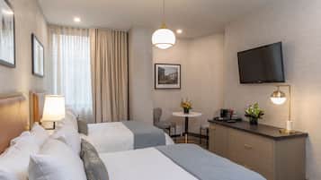 A hotel room with two beds, a desk, a TV, and a window with curtains.