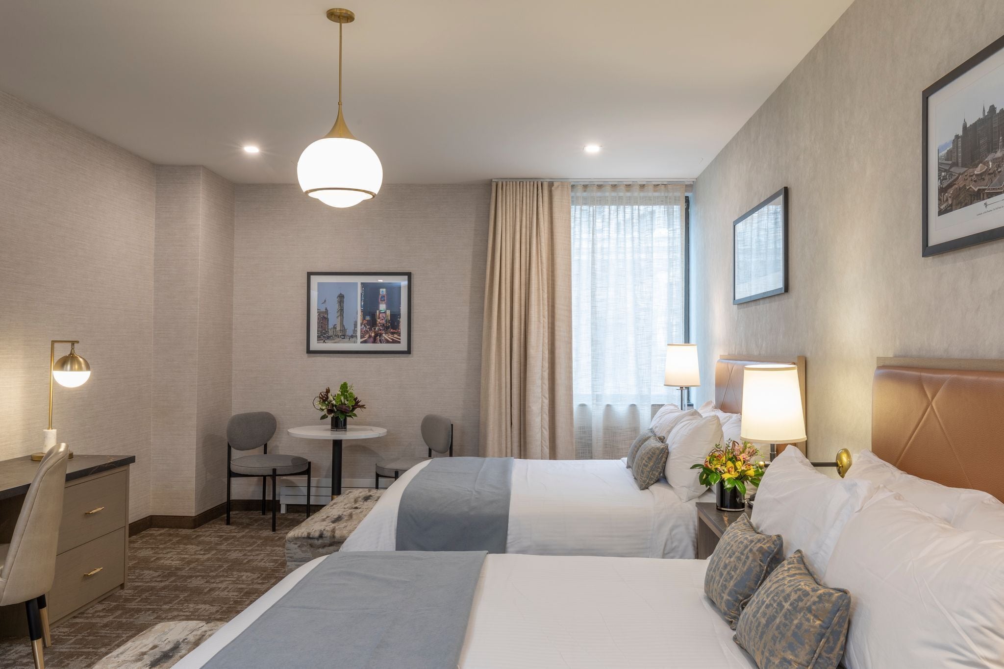 Hotelkamer met twee bedden, een bureau, een stoel, een bijzettafeltje met een plant en een raam met gordijnen.