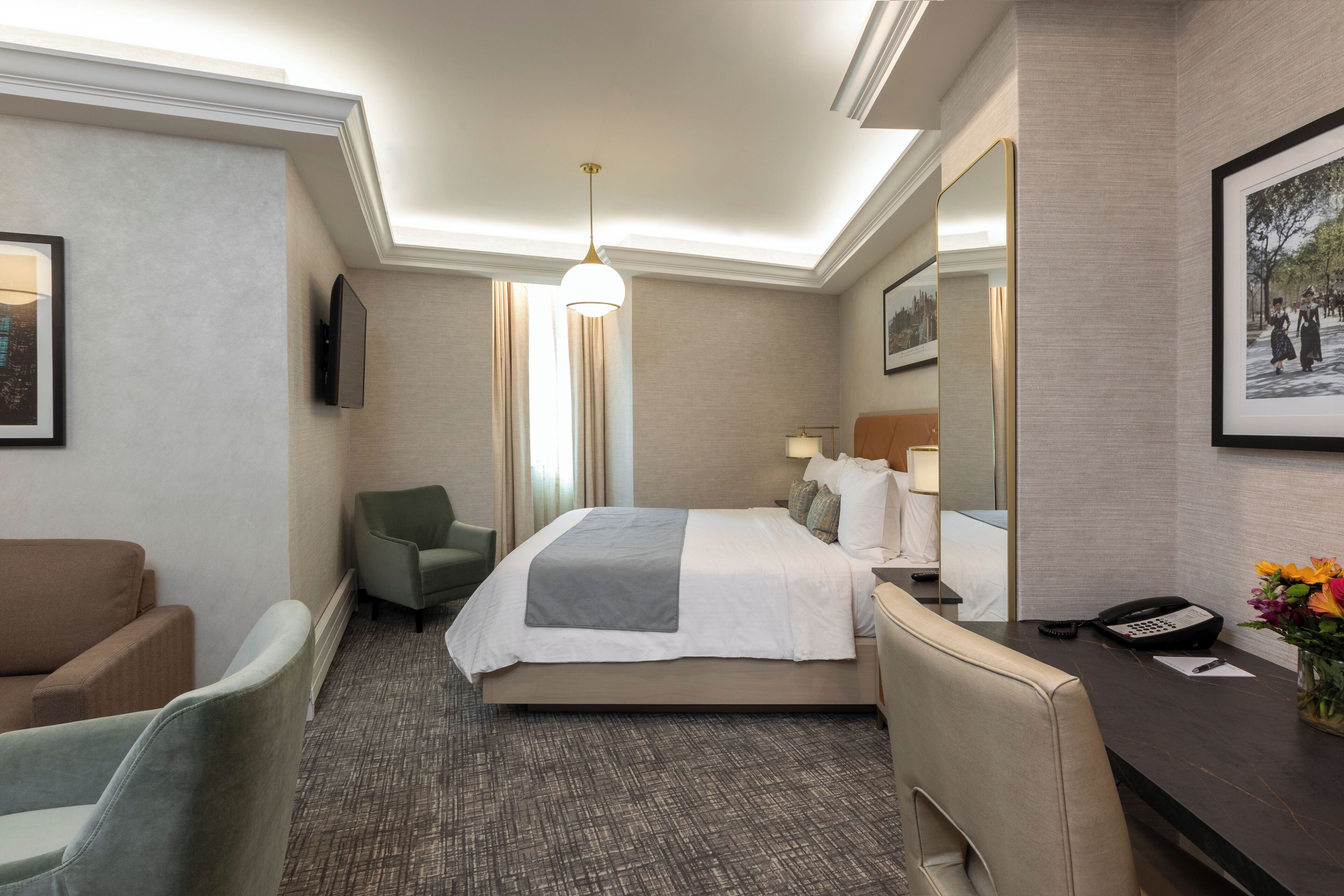 A hotel room with a bed, a desk, a chair, a TV, and a mirror.