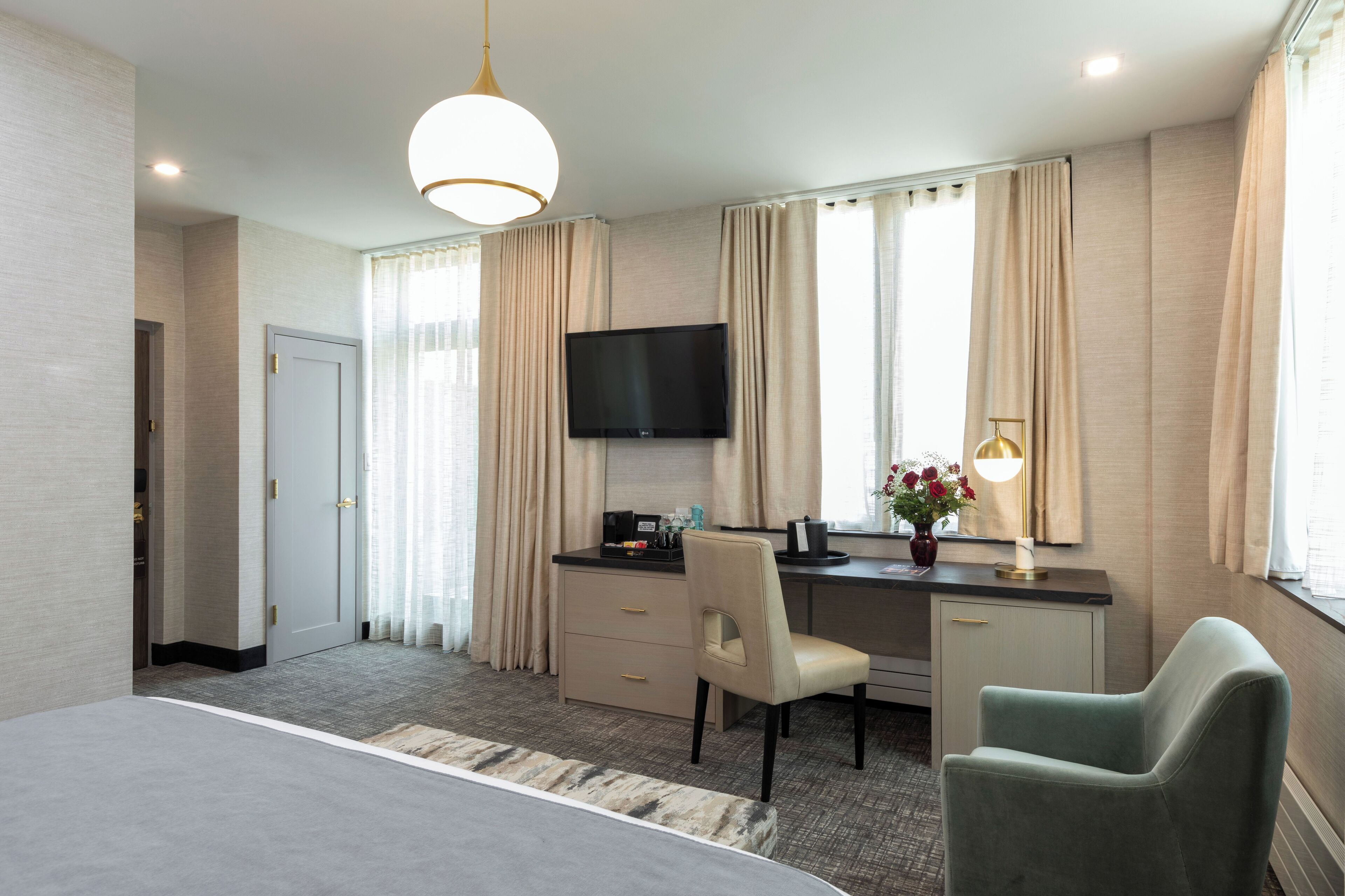 Habitación de hotel con cama, escritorio, silla, televisor y lámpara.