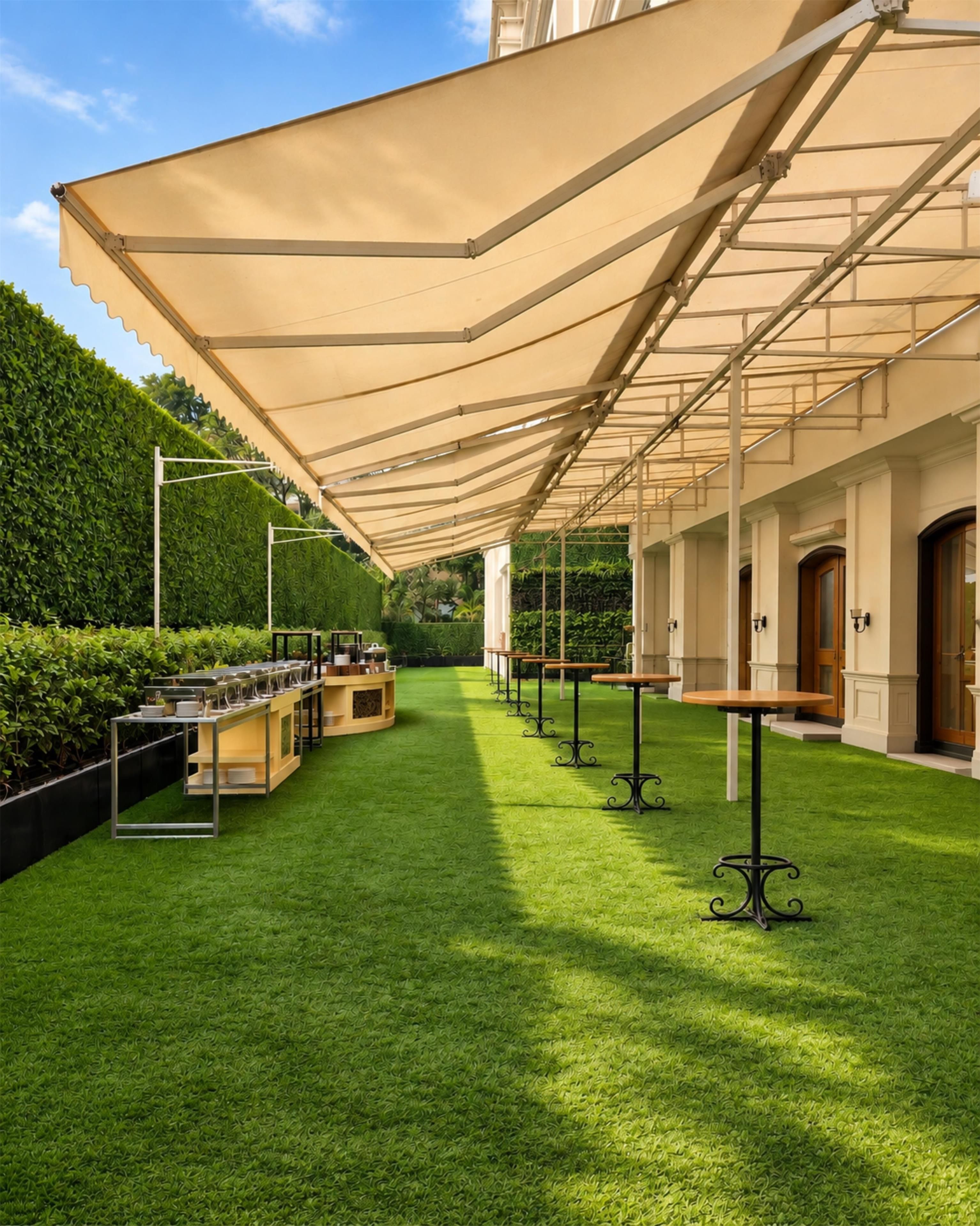 An outdoor patio with a covered seating area, artificial grass, and a backdrop of greenery.