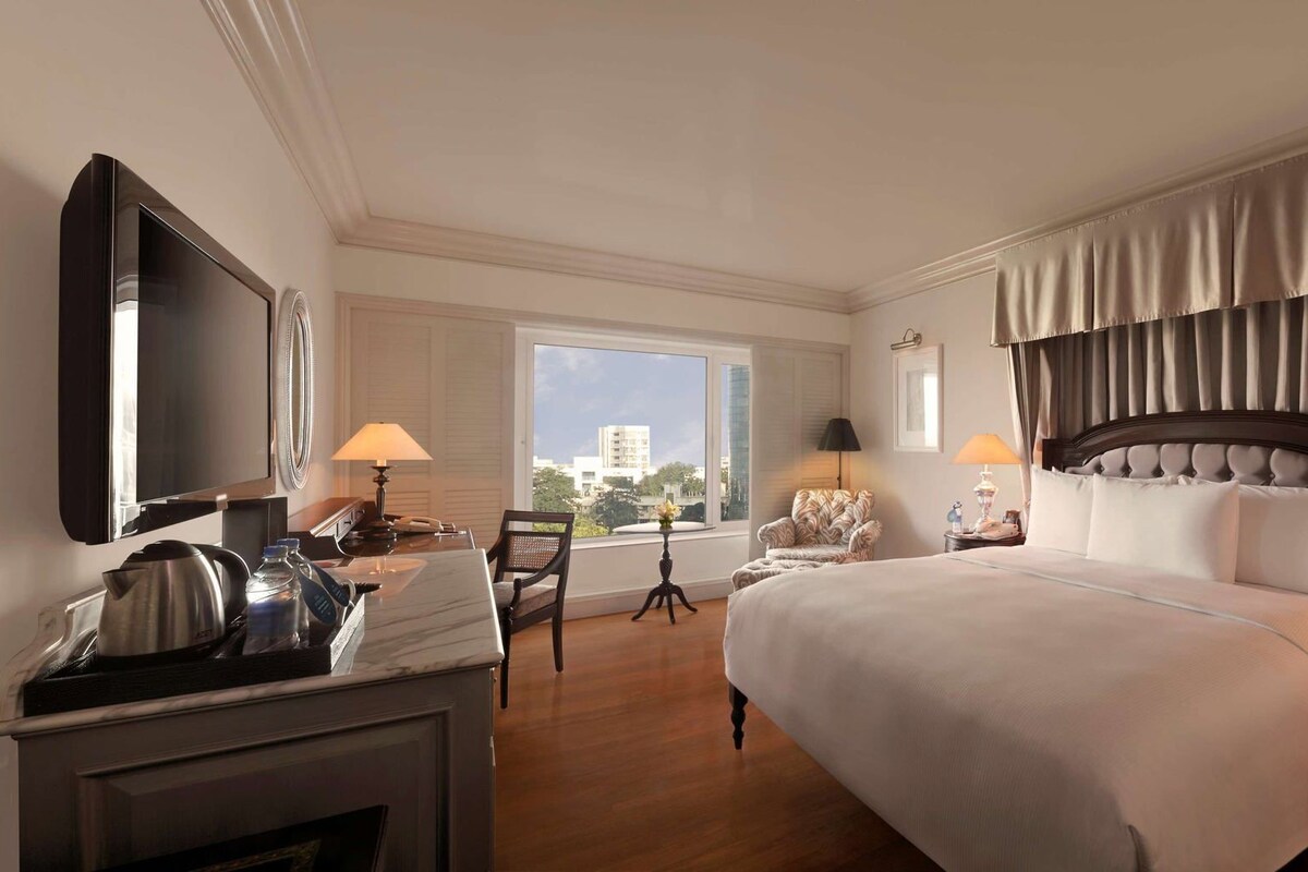 Une chambre d’hôtel avec un grand lit, une télévision, un bureau avec une bouilloire, une chaise et une fenêtre donnant sur la ville.