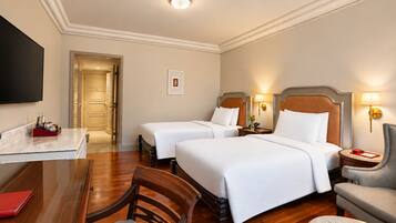 A hotel room with two beds, a desk, a chair, and a television.