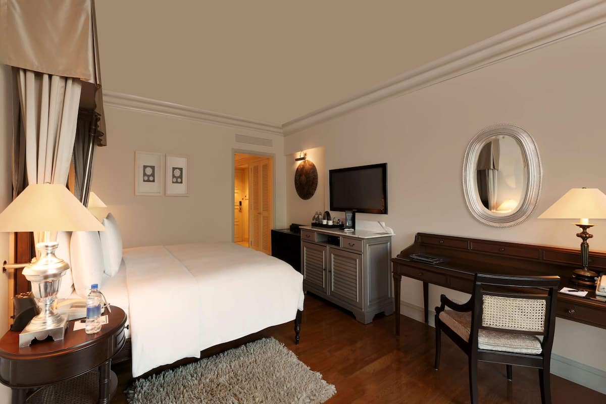 Een hotelkamer met een bed, nachtkastjes, een bureau, een stoel, een televisie en een spiegel.