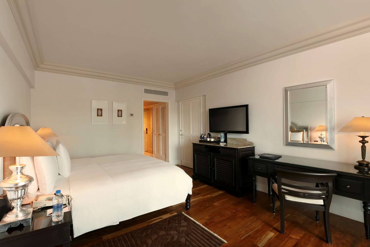Een hotelkamer met een bed, een bureau met stoel, een televisie en een spiegel.