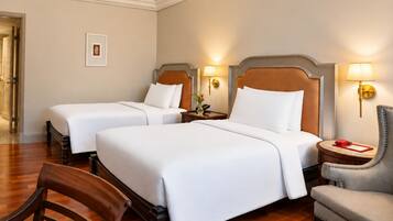 Une chambre d’hôtel avec deux lits, une chaise en bois, une petite table et une lampe.