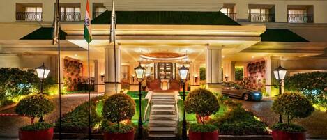 Ingresso di un hotel con una bandiera, gradini che conducono all'ingresso principale e piante in vaso.