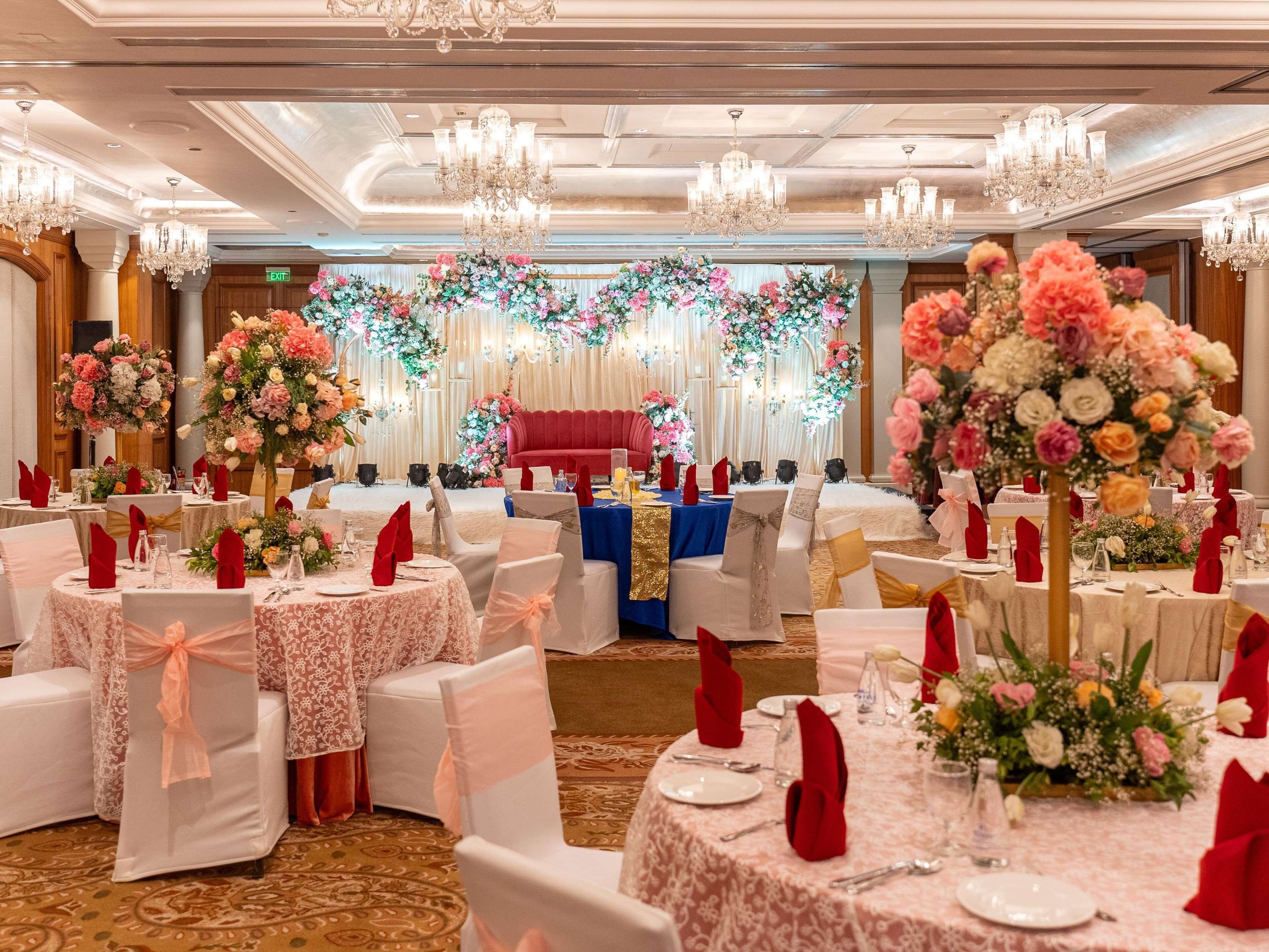 A banquet hall with round tables, white chairs with pink sashes, and floral centerpieces.