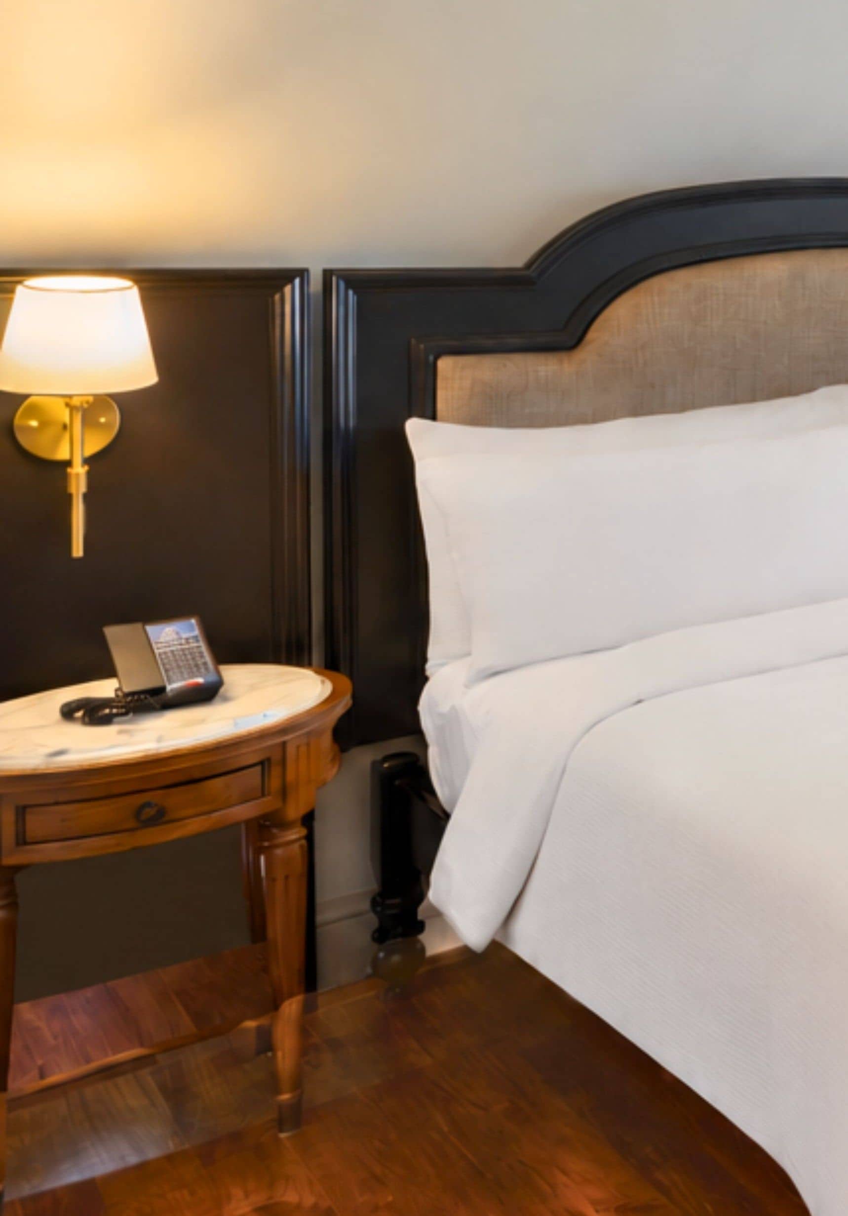A hotel room with a bed, a bedside table with a lamp, and a telephone.