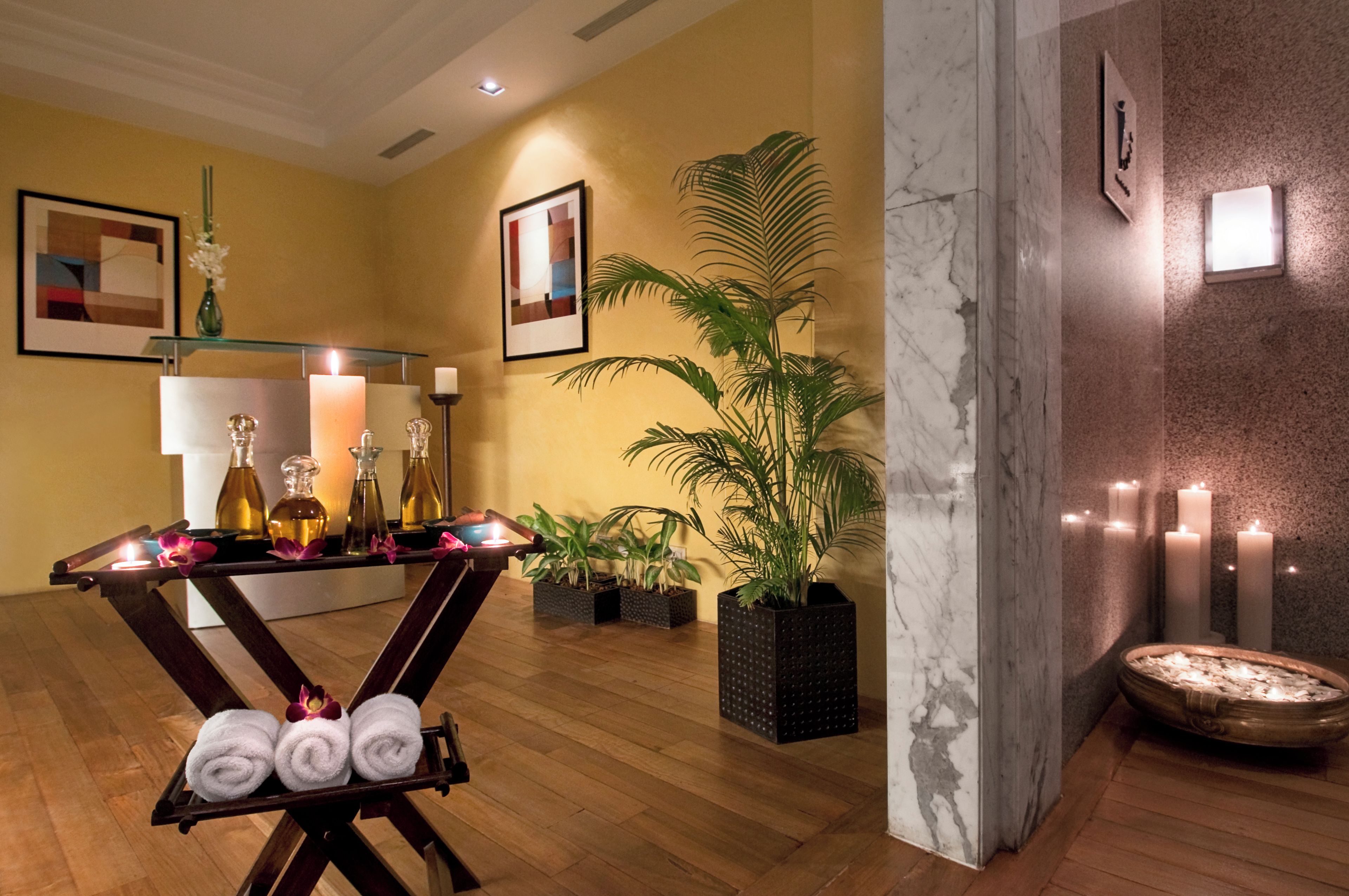 A spa area with a wooden floor, a table with bottles and towels, a potted plant, and candles.