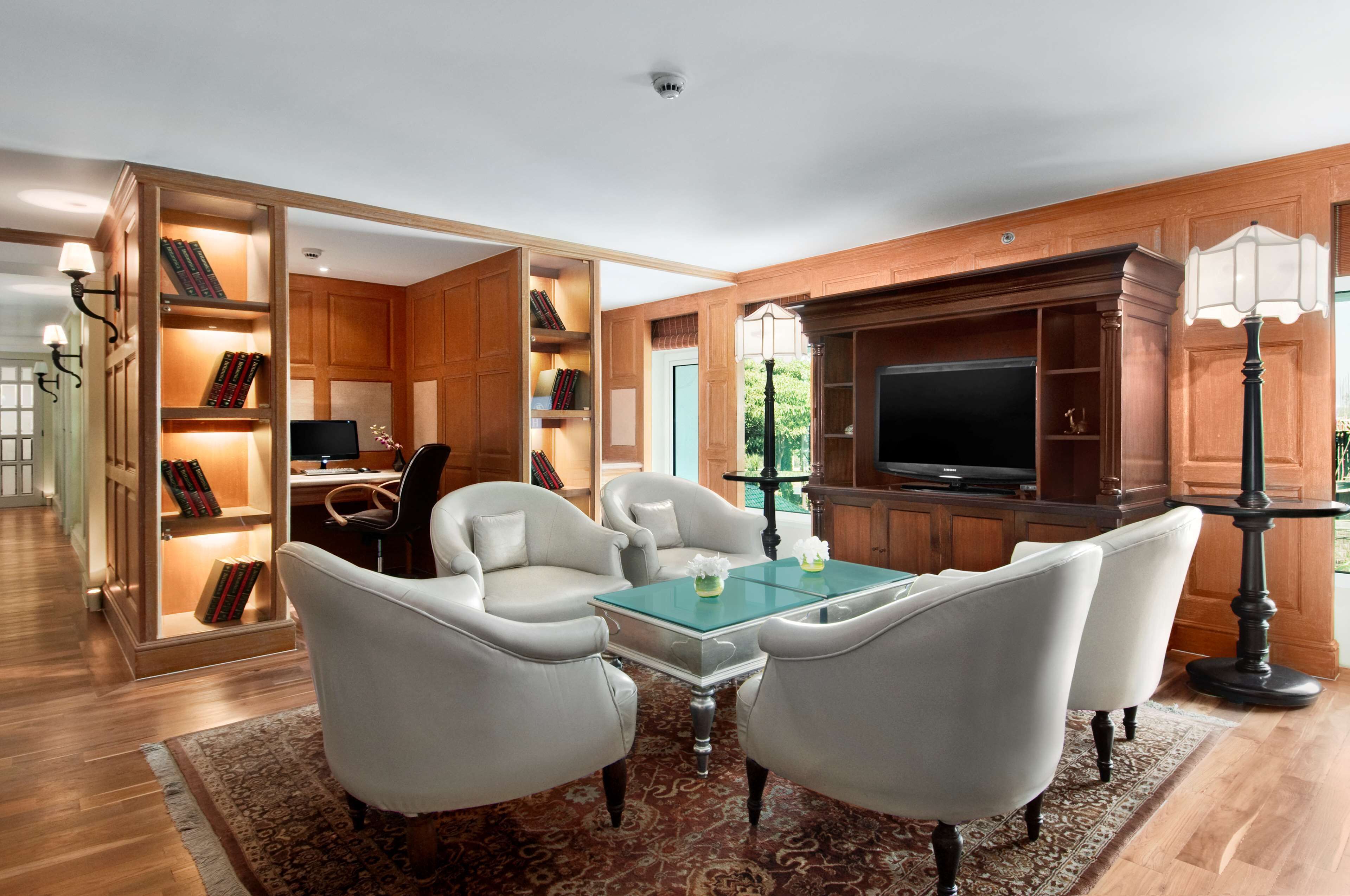 A spacious living room with a large TV, comfortable seating, and a bookshelf filled with books.