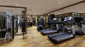 Een sportschool met loopbanden, krachtapparaten en spiegels aan de muur.