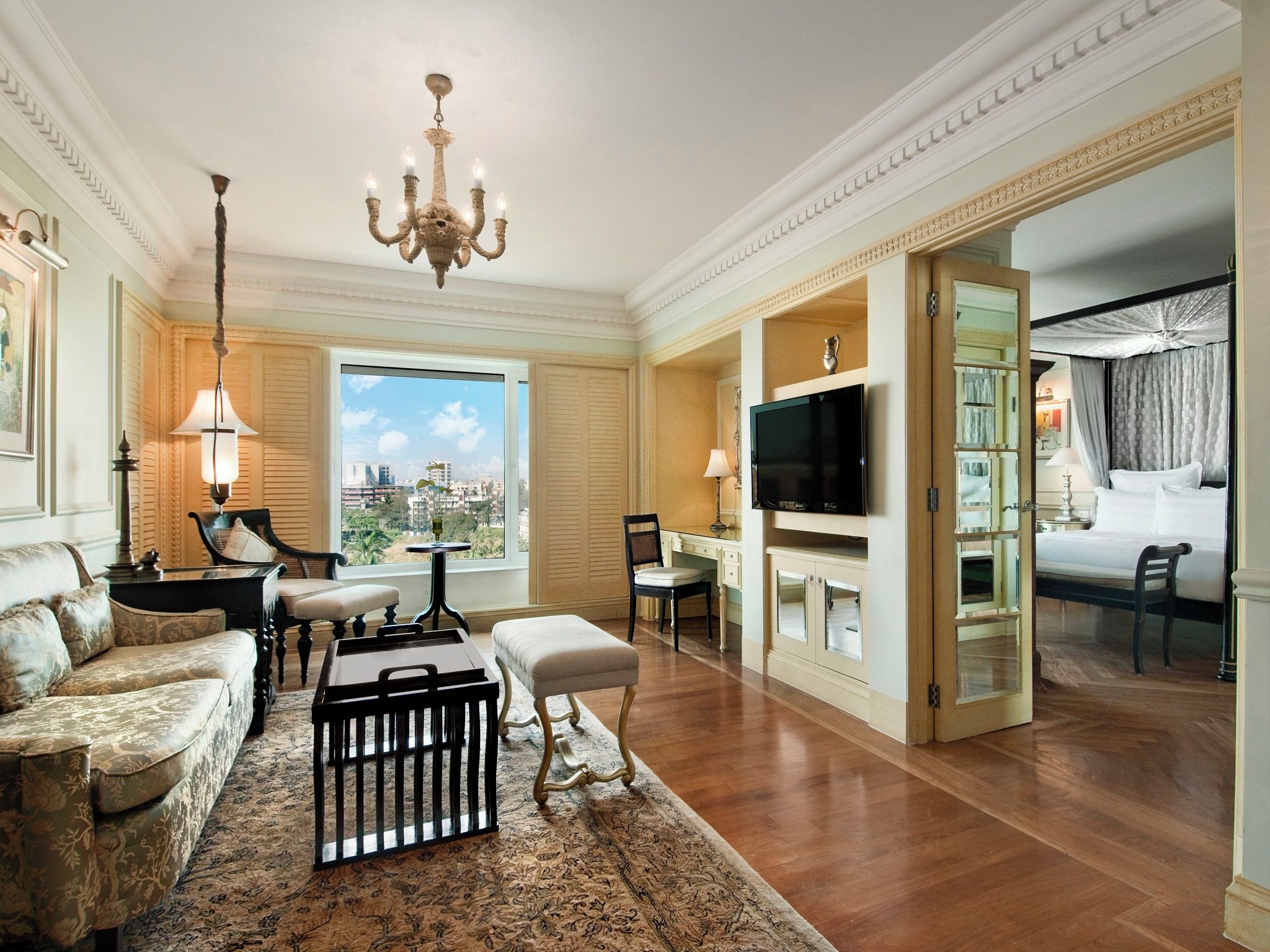 A spacious living room with a large window, a chandelier, a television, and a cozy seating area.