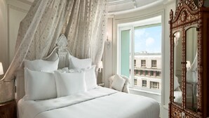 Een luxueuze slaapkamer met hemelbed, een groot versierd spiegel en uitzicht op gebouwen.