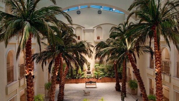 Een ruime atrium met een hoge plafond, palmbomen, een fontein in het midden en een standbeeld.
