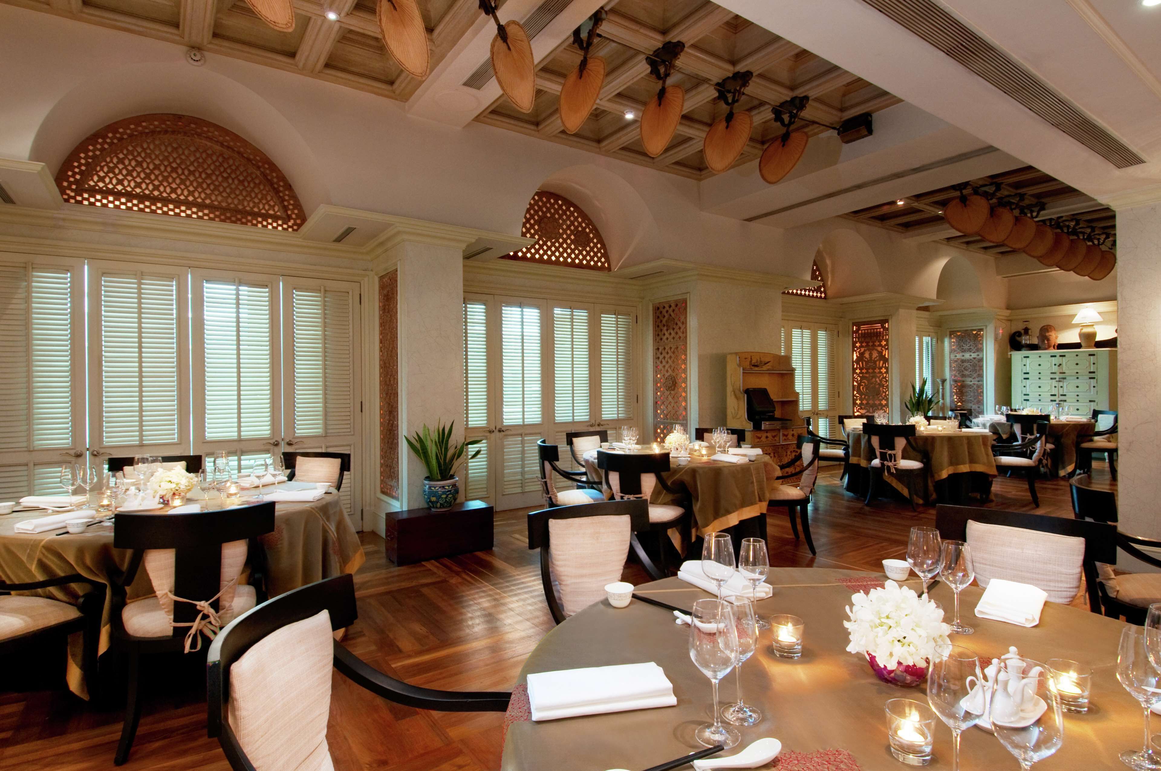 A dining area with multiple tables set for a meal, featuring white tablecloths, candles, and floral centerpieces.