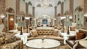 Eine luxuriöse Lobby mit einem prunkvollen Kronleuchter, bequemen Sitzmöglichkeiten und Marmorböden.