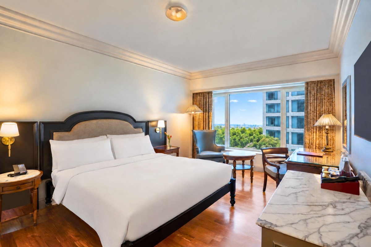 Une chambre d’hôtel avec un grand lit, un bureau, une chaise et une vue sur le paysage urbain.