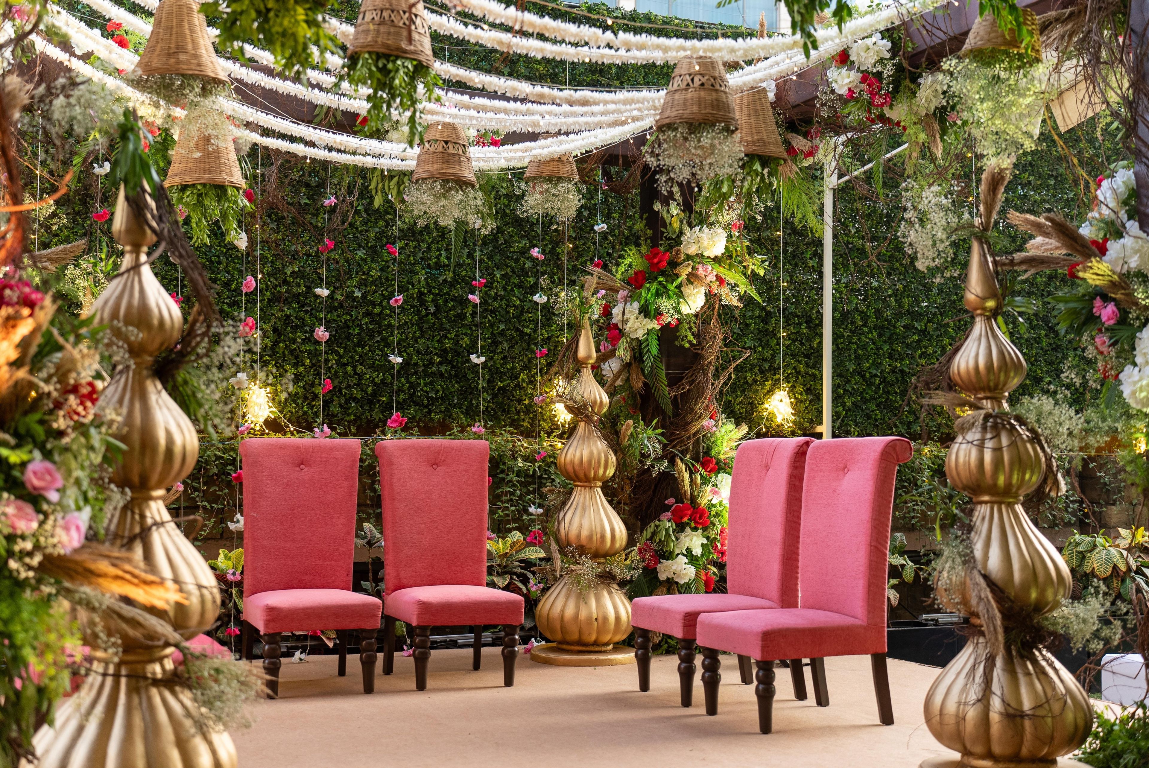 Un área de estar con dos sillones y jarrones decorativos, rodeada de abundante follaje y arreglos florales colgantes.