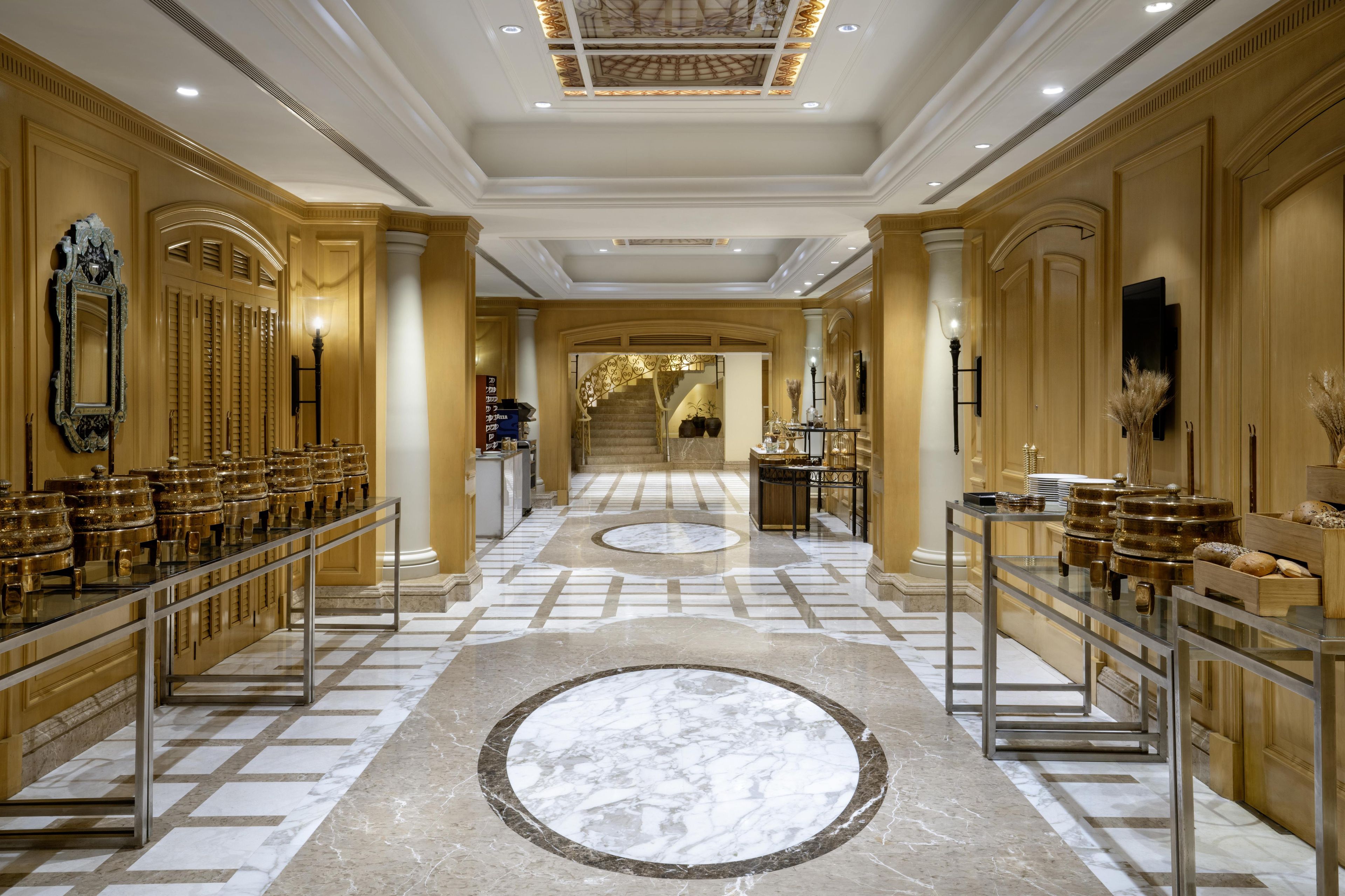 A grand hallway with marble flooring, gold accents, and a central circular marble design.
