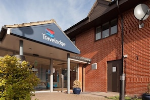 Eingang eines Travelodge Hotels mit überdachtem Gang, Satellitenschüssel und einer Fassade aus Backsteinen.