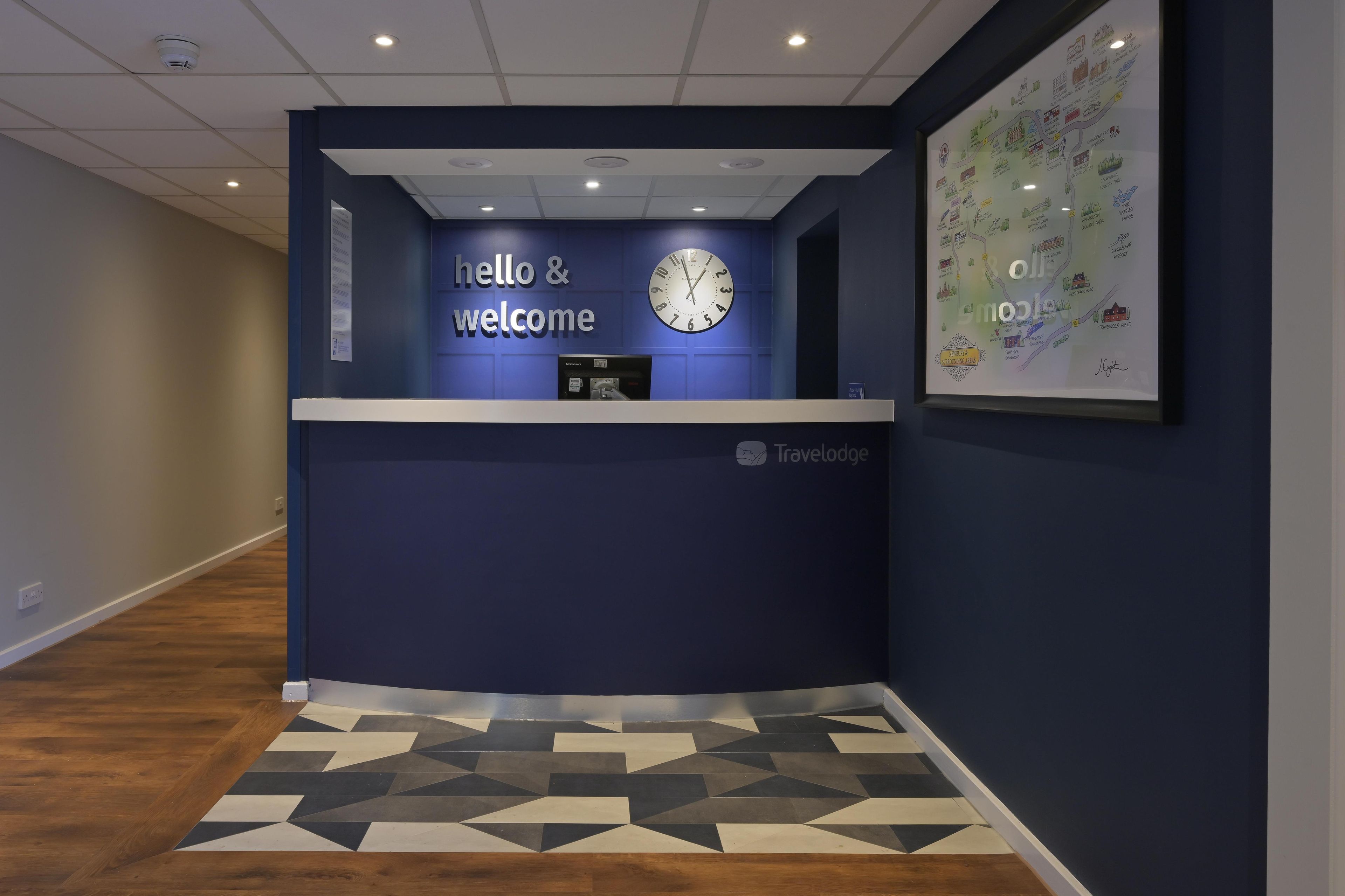 Ein Empfangsschalter mit einer Uhr, einem 'hello & welcome' Schild und einer gerahmten Karte an der Wand.