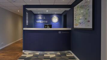 Ein Empfangsschalter mit einer Uhr, einem 'hello & welcome' Schild und einer gerahmten Karte an der Wand.