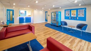 A hotel lobby with a reception desk, seating areas, a vending machine, and informational posters on the walls. - Travelodge Colchester Feering (Colchester)