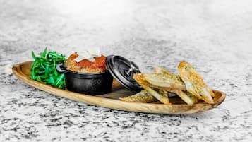 A wooden tray with a black bowl, a piece of bread, and green salad on a marble surface.