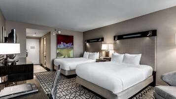 A hotel room with two beds, a desk, a chair, and a painting on the wall.