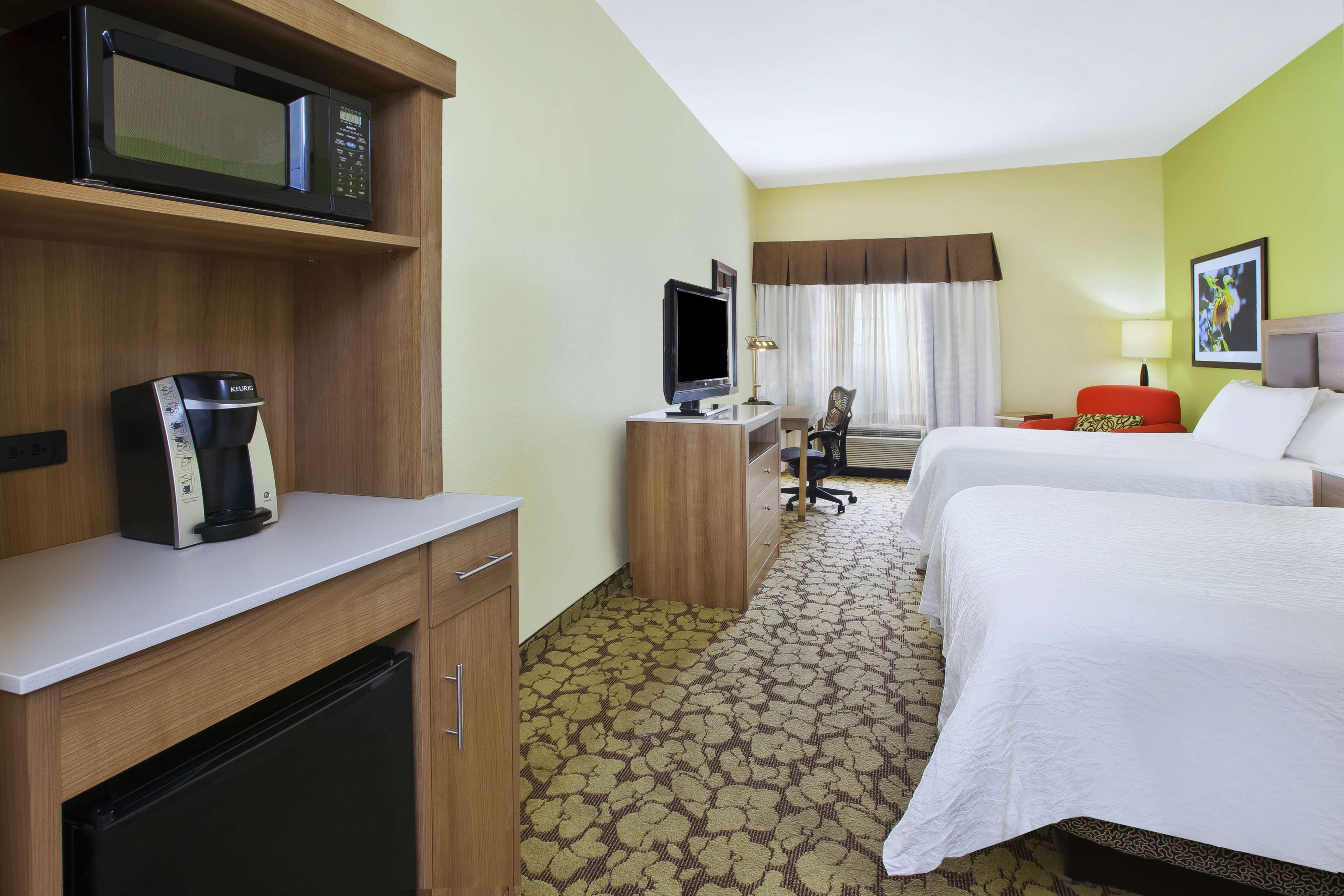A hotel room with a kitchenette, a television, a desk, a chair, two beds, and a window with curtains.