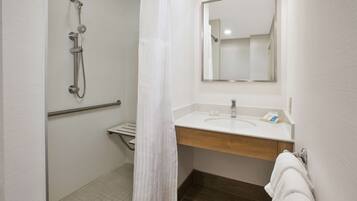 A bathroom with a shower, a sink, a mirror, and a towel rack.