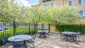An outdoor patio area with round tables and chairs, a fence, and a building labeled "Hilton Garden Inn" in the background. - Hilton Garden Inn Wichita (Wichita)