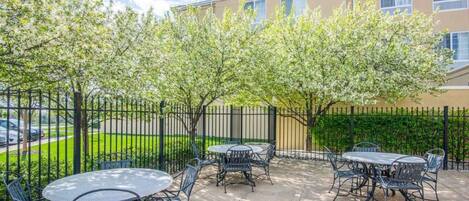 An outdoor patio area with round tables and chairs, a fence, and a building labeled "Hilton Garden Inn" in the background.