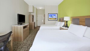 A hotel room with two beds, a desk with a television, a chair, and a lamp.