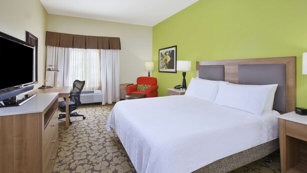 A hotel room with a bed, desk, chair, TV, and a window with curtains.