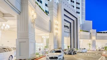 Imponente ingresso di un hotel con un'ampia arcata, diverse auto parcheggiate davanti e una facciata ben illuminata.