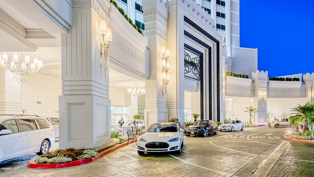 A hotel entrance with a grand facade, multiple entry points, and a parking area with several cars.