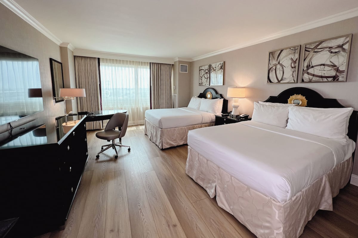 Una habitación de hotel con dos camas, un escritorio con una silla, un televisor y obras de arte en las paredes.