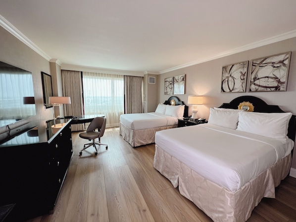 Una habitación de hotel con dos camas, un escritorio con una silla, un televisor y obras de arte en las paredes.