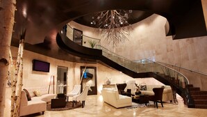 A spacious lobby with a curved staircase, a large chandelier, and a modern interior design.