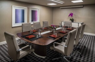 A conference room with a long table, chairs, a small side table, and a potted plant.
