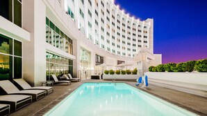 A modern hotel with a large indoor pool, sun loungers, and a well-lit exterior.
